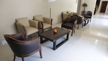 A modern hotel lobby with a seating area featuring leather sofas and armchairs, a coffee table with a decorative item, and a tall floor lamp.