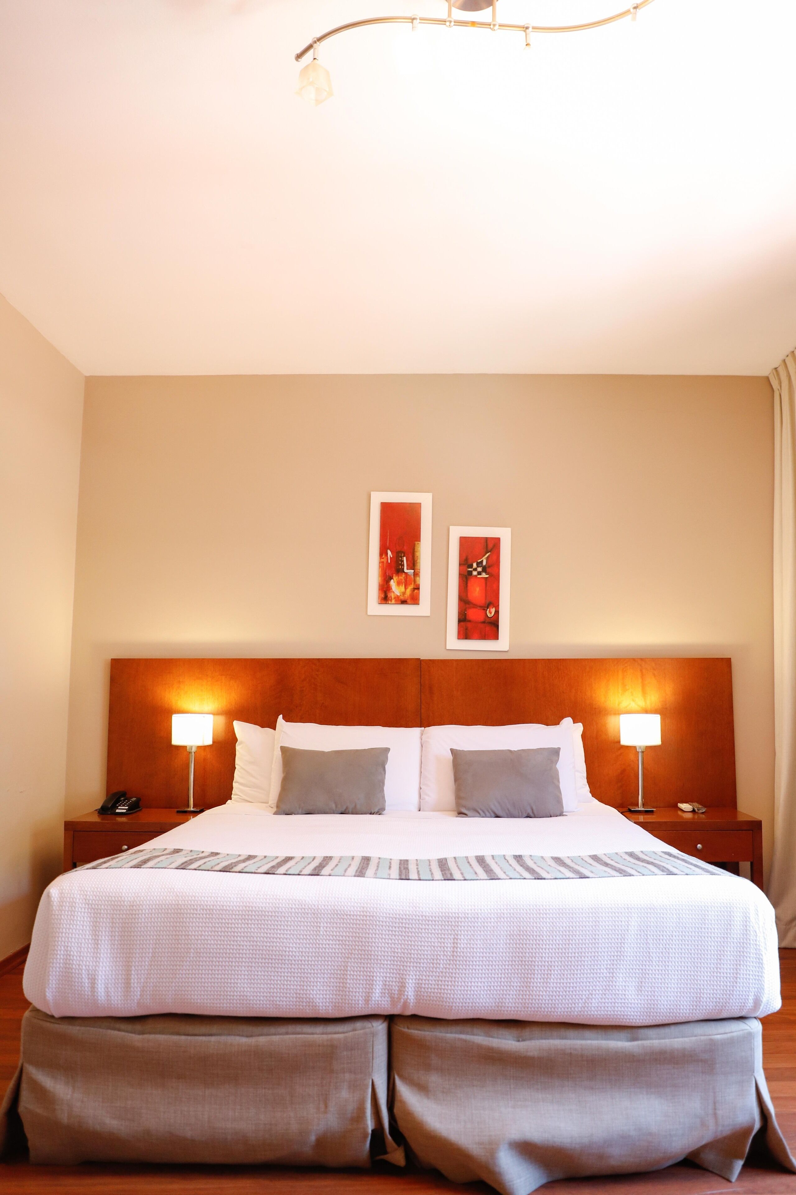 A hotel room with a large bed, two bedside lamps, and two framed pictures on the wall.