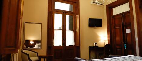 Una habitación de hotel con una cama, una silla, una mesita, un televisor y una araña.