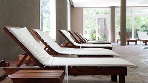 A row of wooden sun loungers with white cushions in a spacious indoor area with large windows. - Howard Johnson by Wyndham Escobar Hotel (Belen de Escobar)