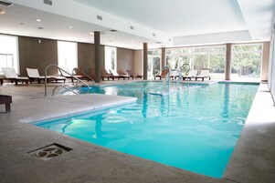 Una piscina interior con agua cristalina, rodeada de sillones de descanso y amplios ventanales.