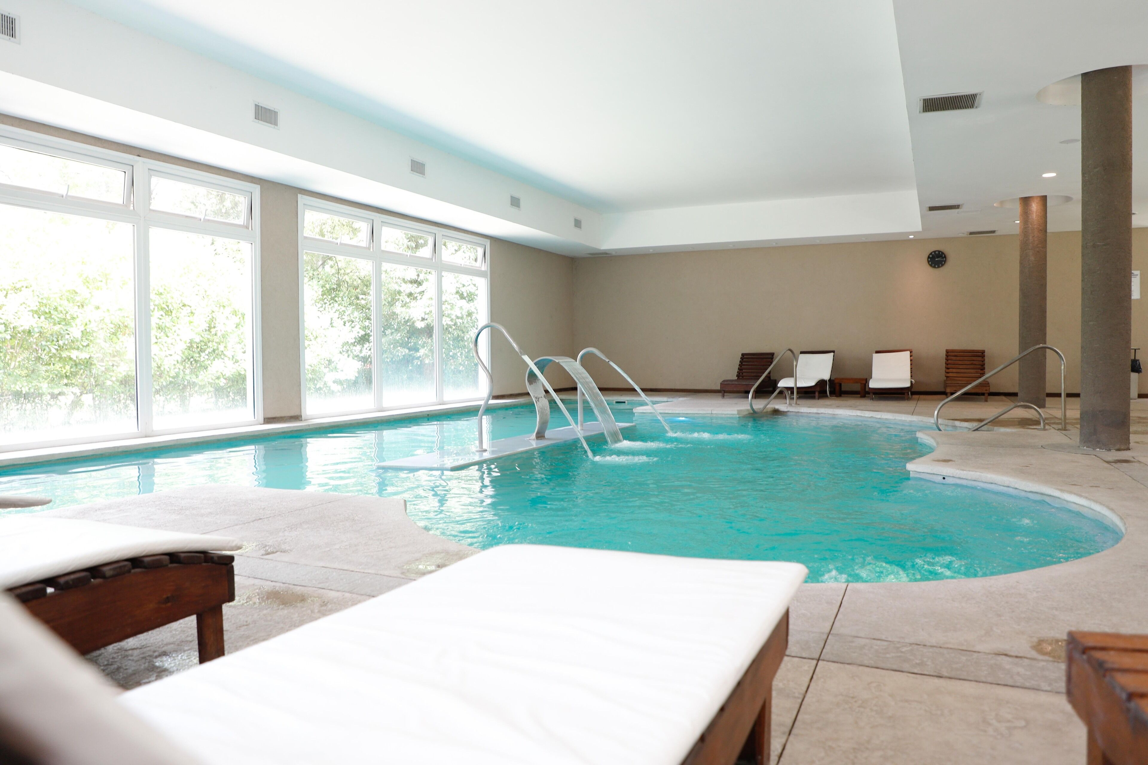 A large indoor swimming pool with clear blue water, surrounded by lounge chairs and a sunbed.