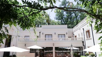 Un edificio con fachada blanca, un balcón, mobiliario exterior con sombrillas y un jardín bien cuidado.