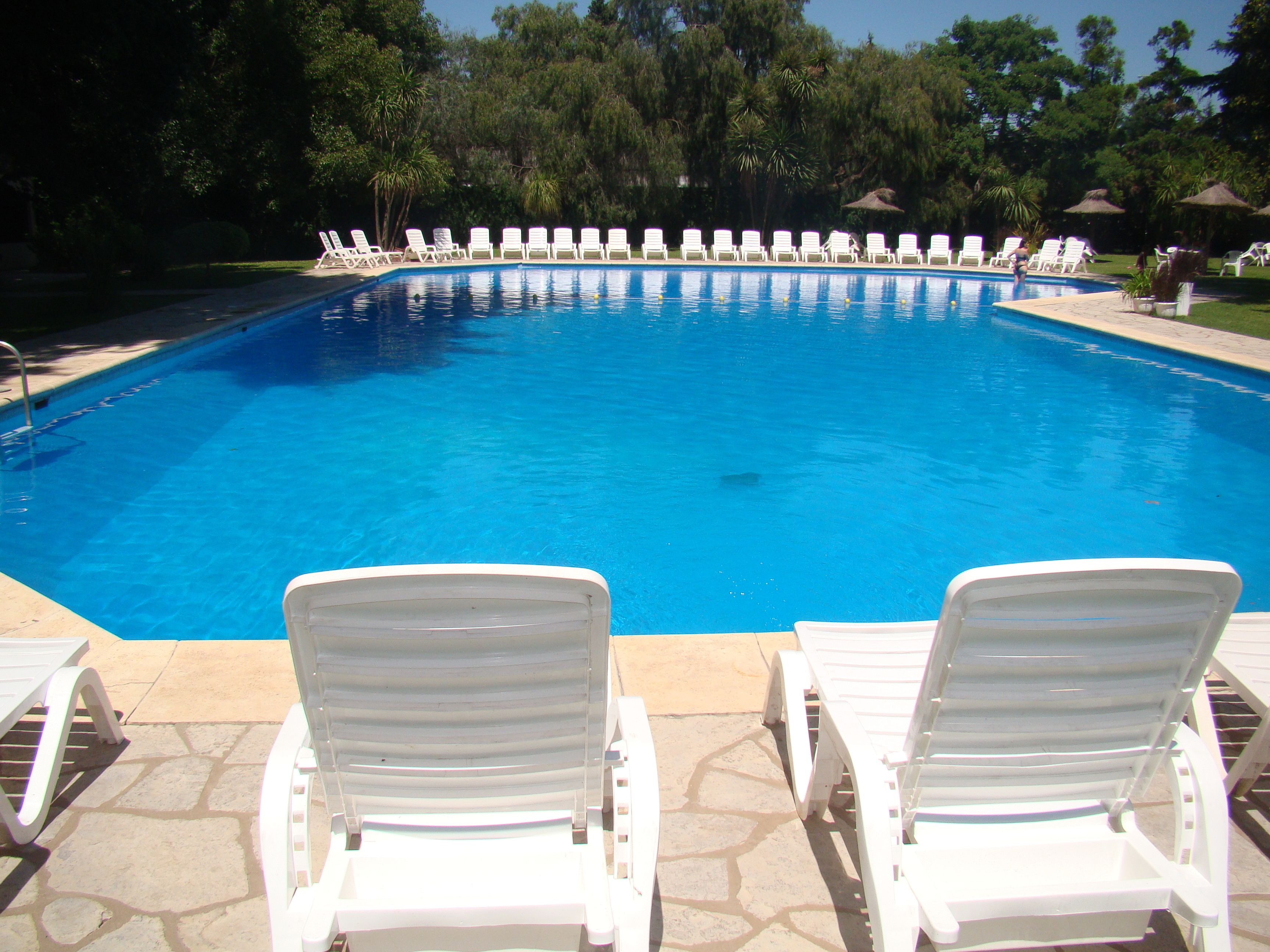 A swimming pool with white lounge chairs in the foreground and a line of white chairs along the poolside.