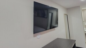 A room with a flat-screen TV mounted on the wall, a mirror, and a dark wooden table. - Travelodge by Wyndham Buena Park (Buena Park)