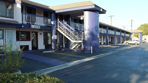A motel with a central staircase, a covered parking area, and a sign indicating an office. - Travelodge by Wyndham Buena Park (Buena Park)