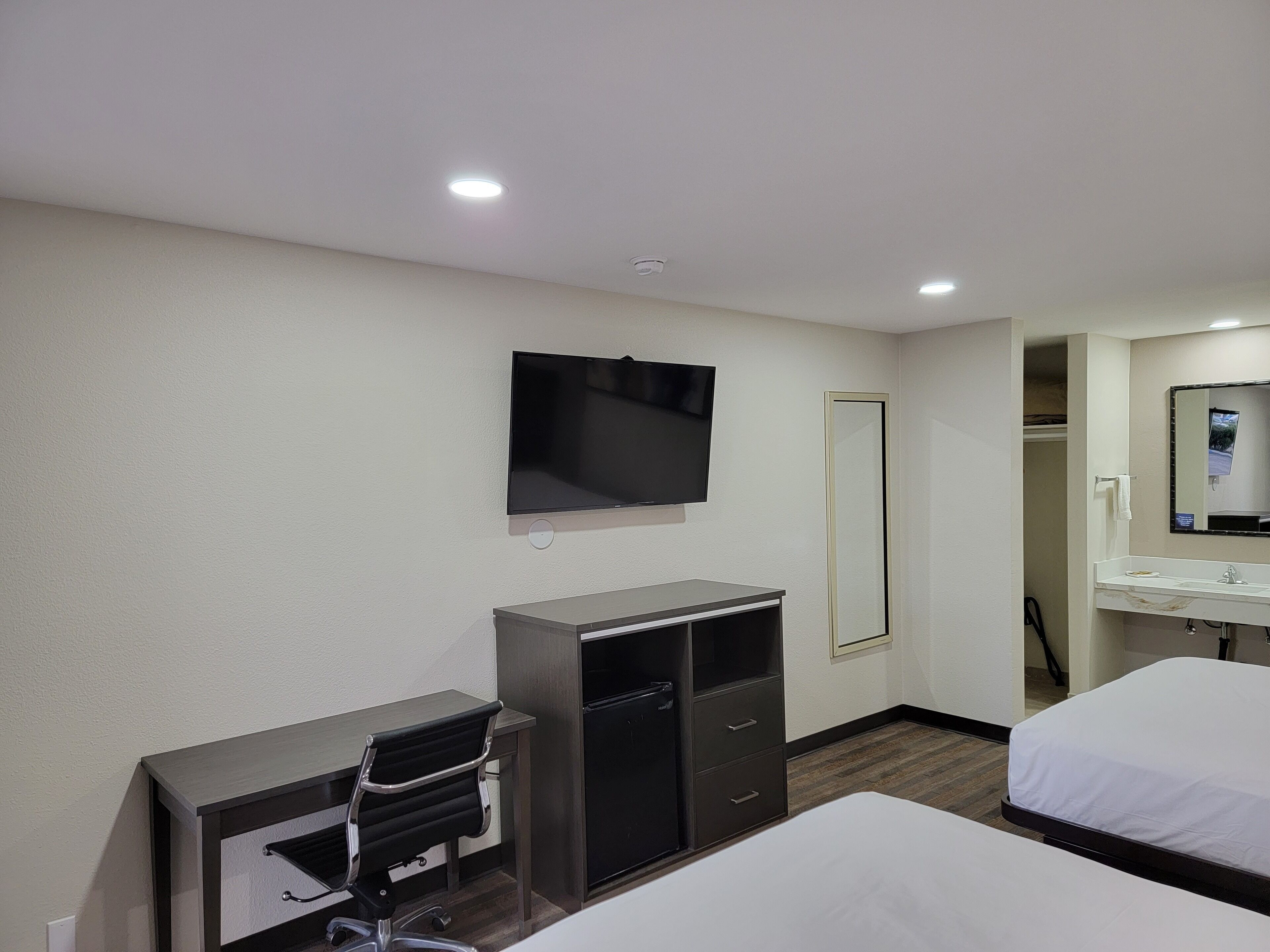 Una habitación de hotel con una cama, un escritorio con silla, un televisor, un espejo y un armario.