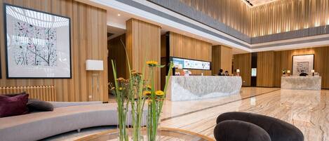 En modern hotellobby med en receptionsdisk, en sittgrupp och en stor, abstrakt målning.