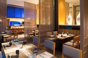 Un espace de restauration moderne avec des tables prévues pour deux personnes, où l’on trouve un mélange de chaises en bois et de chaises rembourrées.