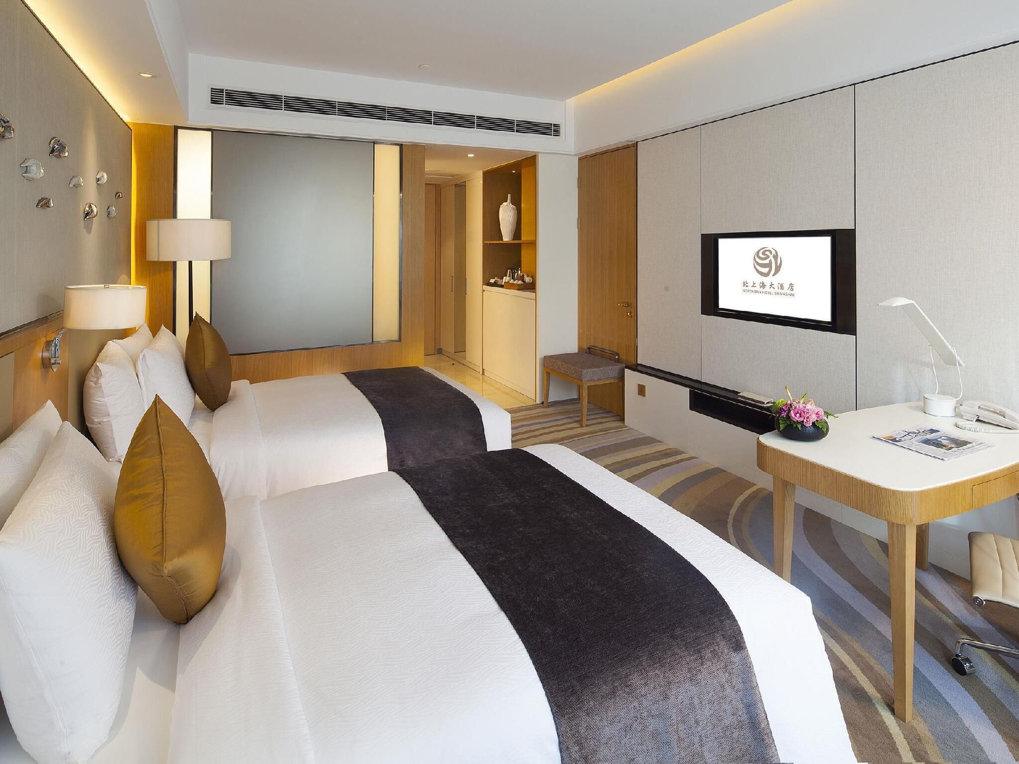 A hotel room with two beds, a desk, a TV, and a bathroom.