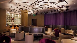 A modern lounge area with leather seating, a bar with bottles, and a stage with curtains.