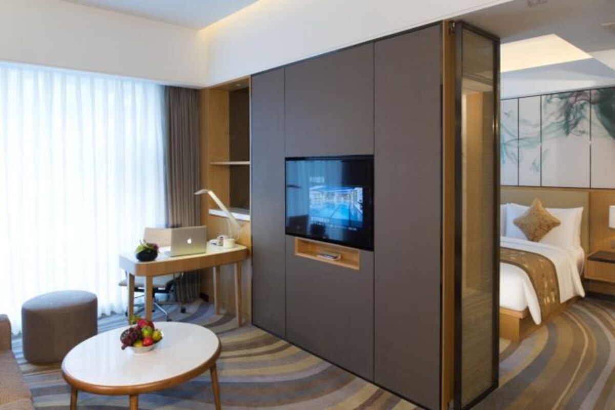 A hotel room with a bed, a desk with a laptop, a television, and a fruit bowl.