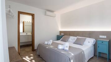 Un dormitorio con cama, mesitas de noche, un espejo y un perchero.