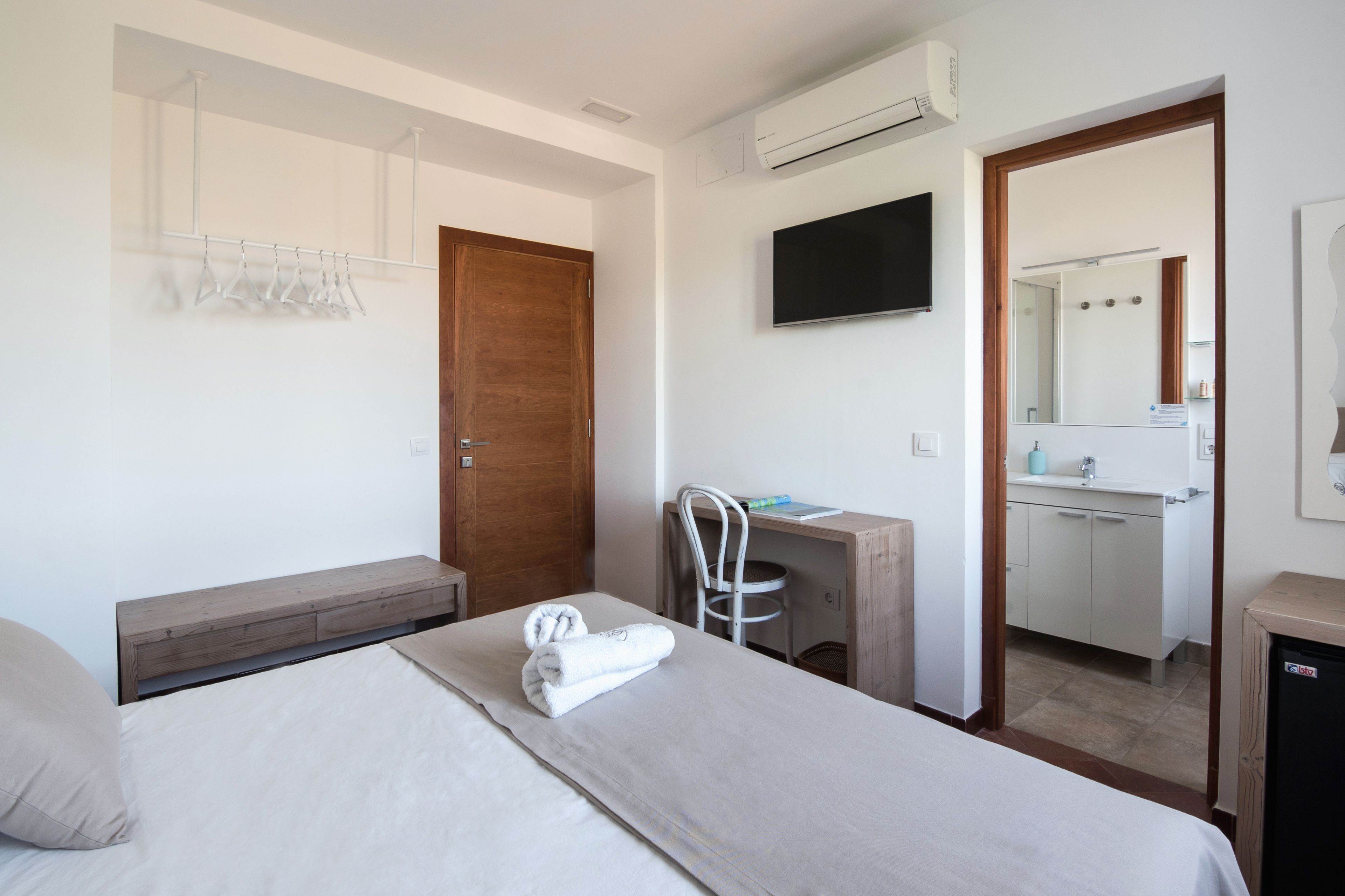 Quarto de hotel com uma cama, uma mesa, uma cadeira, uma televisão e um banheiro visível por uma porta aberta.