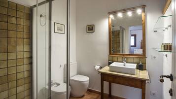 A bathroom with a glass shower enclosure, a white toilet, a wooden vanity with a sink, and a mirror with lights.