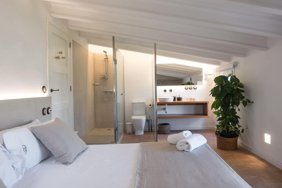 Ett modernt hotellrum med en säng, en dusch, en toalett, ett handfat och en stor krukväxt.