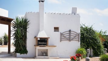 Un edificio blanco con un horno de ladrillo, rodeado de macetas con plantas y flores.