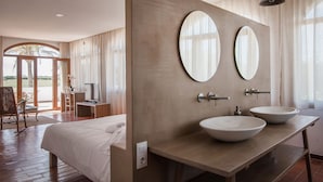 A modern hotel room with a large bed, a wooden vanity with two sinks, and a large mirror.