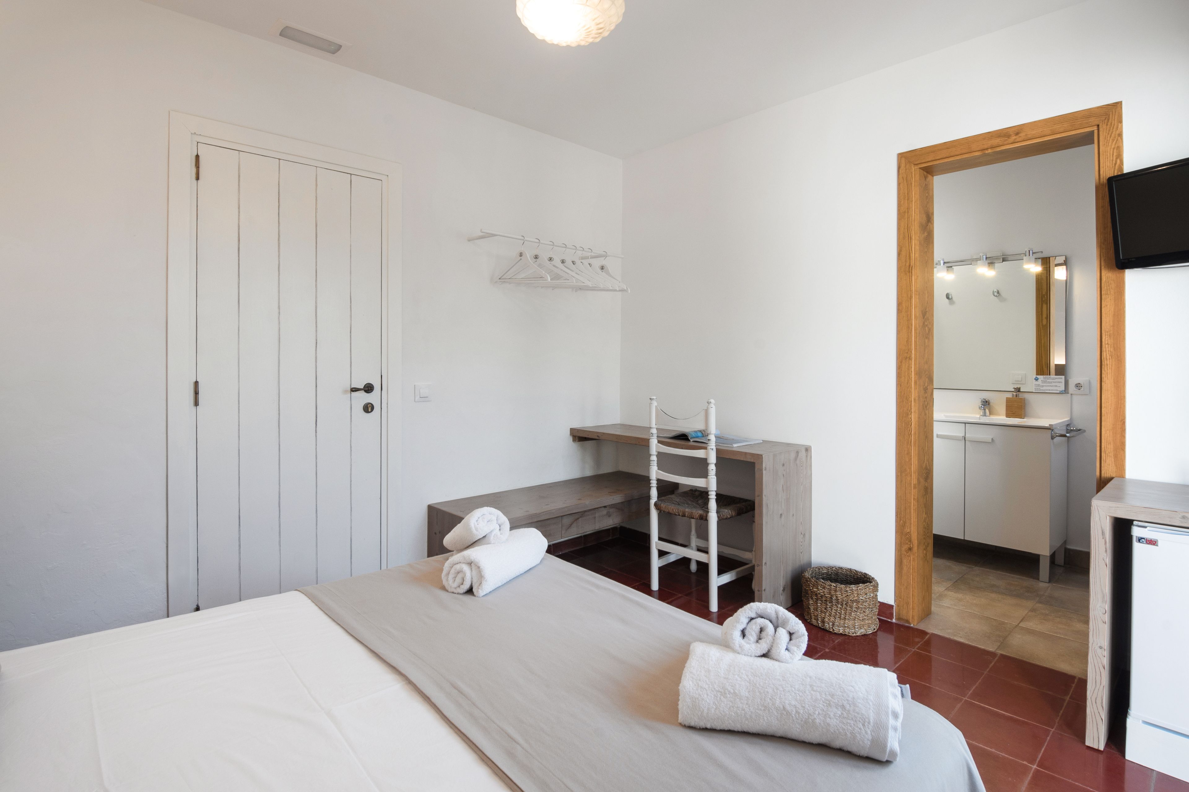 A hotel room with a bed, a desk, a chair, a mirror, a TV, and a bathroom visible through an open door.