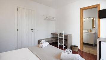 A hotel room with a bed, a desk, a chair, a mirror, a TV, and a bathroom visible through an open door.