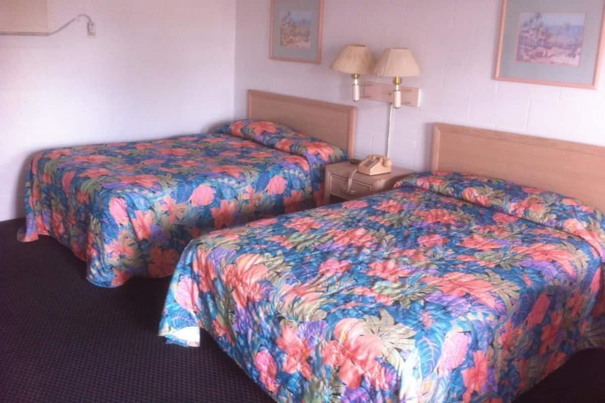 A hotel room with two beds, each with a floral bedspread, a bedside table with a lamp, and a phone.