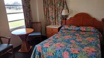 A hotel room with a bed, a desk, a chair, and a window with curtains.