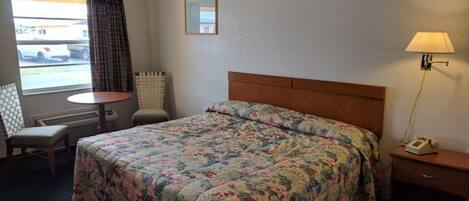 Habitación de hotel con cama, escritorio, silla, lámpara y ventana con cortinas.