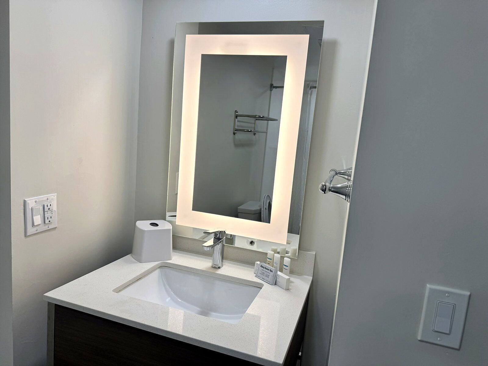 Een badkamer met een witte wastafel, een spiegel met verlichting, een handdoekhouder en een toilet.