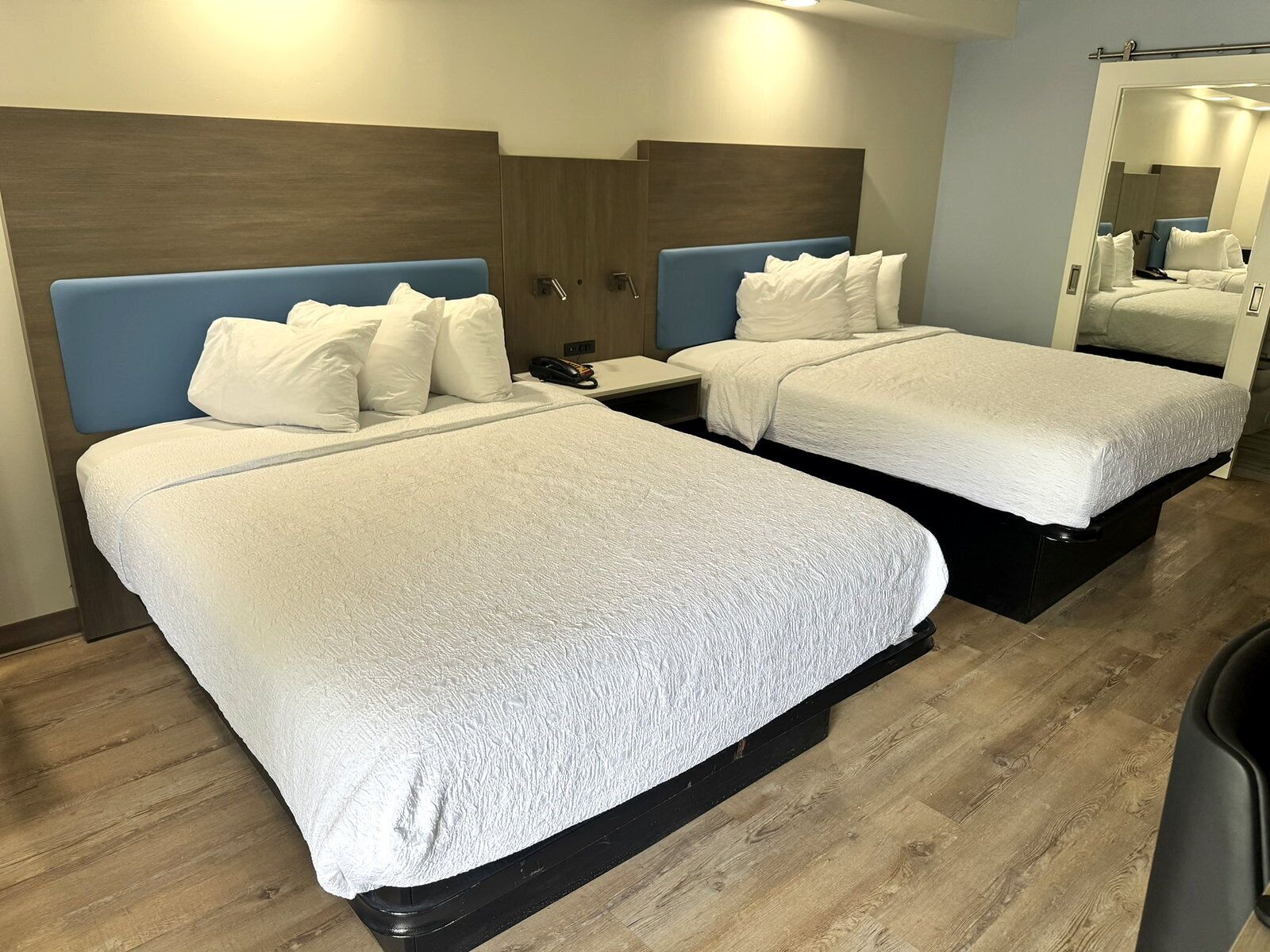 A hotel room with two beds, wooden headboards, white bedding, a bedside table with a phone, and a mirror.