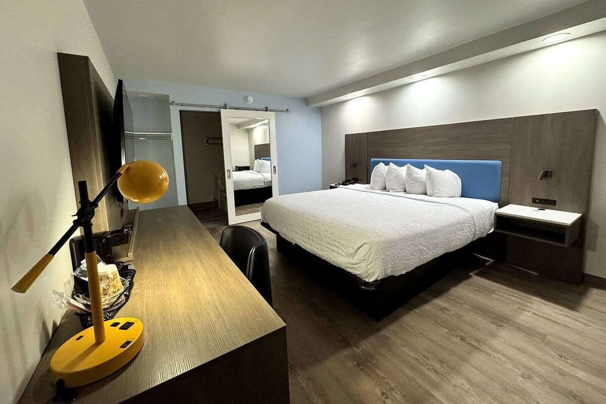A hotel room with a bed, bedside table, lamp, desk, and a mirror.