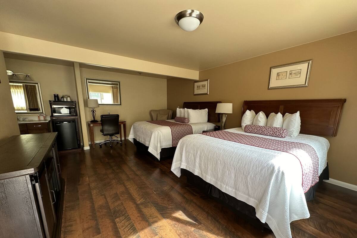 A hotel room with two beds, a desk with a chair, a microwave, and a small kitchenette.