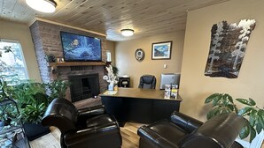 A cozy living room with a fireplace, leather sofas, a TV, and various plants.