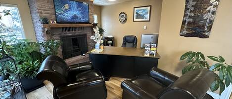 A cozy living room with a fireplace, leather sofas, a TV, and various plants.