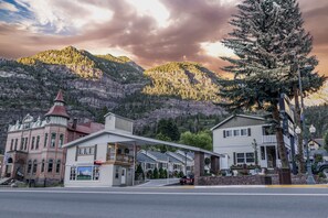 A historic building with a red roof and a balcony, adjacent to a white building with a porch and a signboard. - Abram Inn & Suites (Ouray)