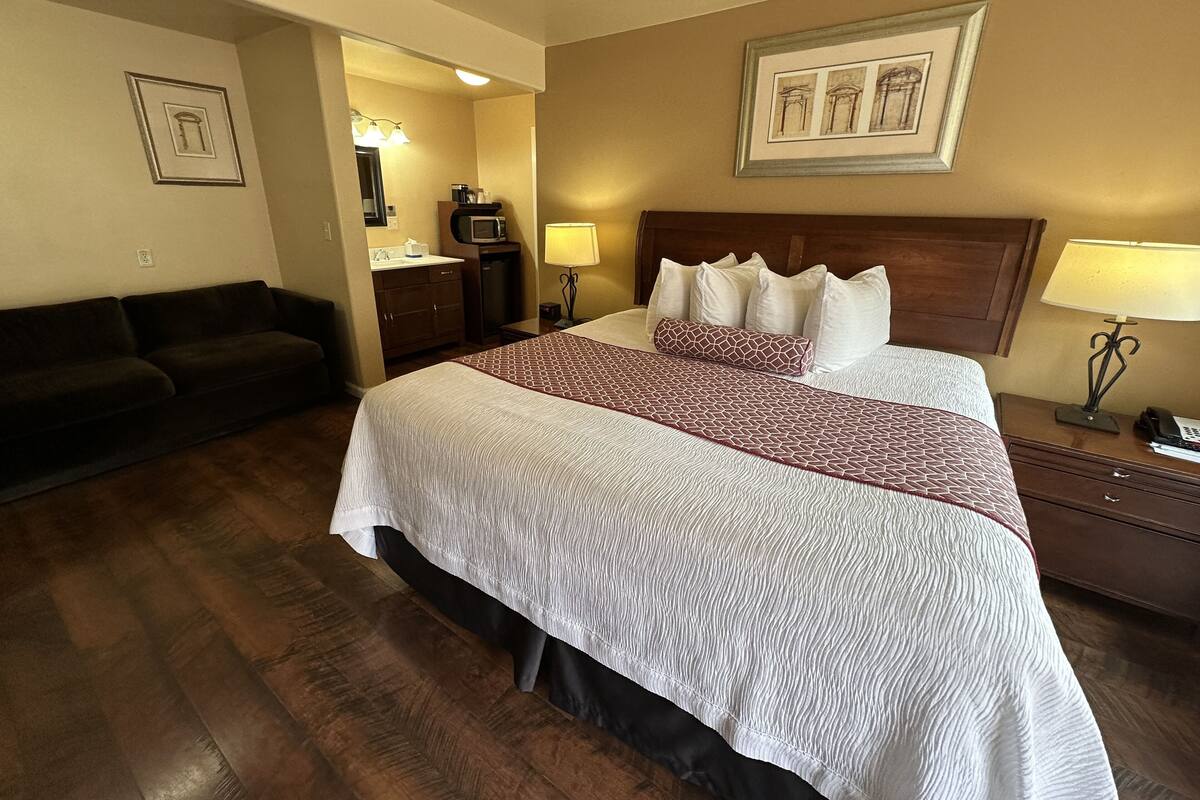 A hotel room with a large bed, a sofa, a desk with a lamp, and a framed picture on the wall.