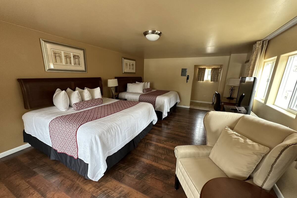 A hotel room with two beds, a sofa, wooden flooring, and framed artwork on the walls.