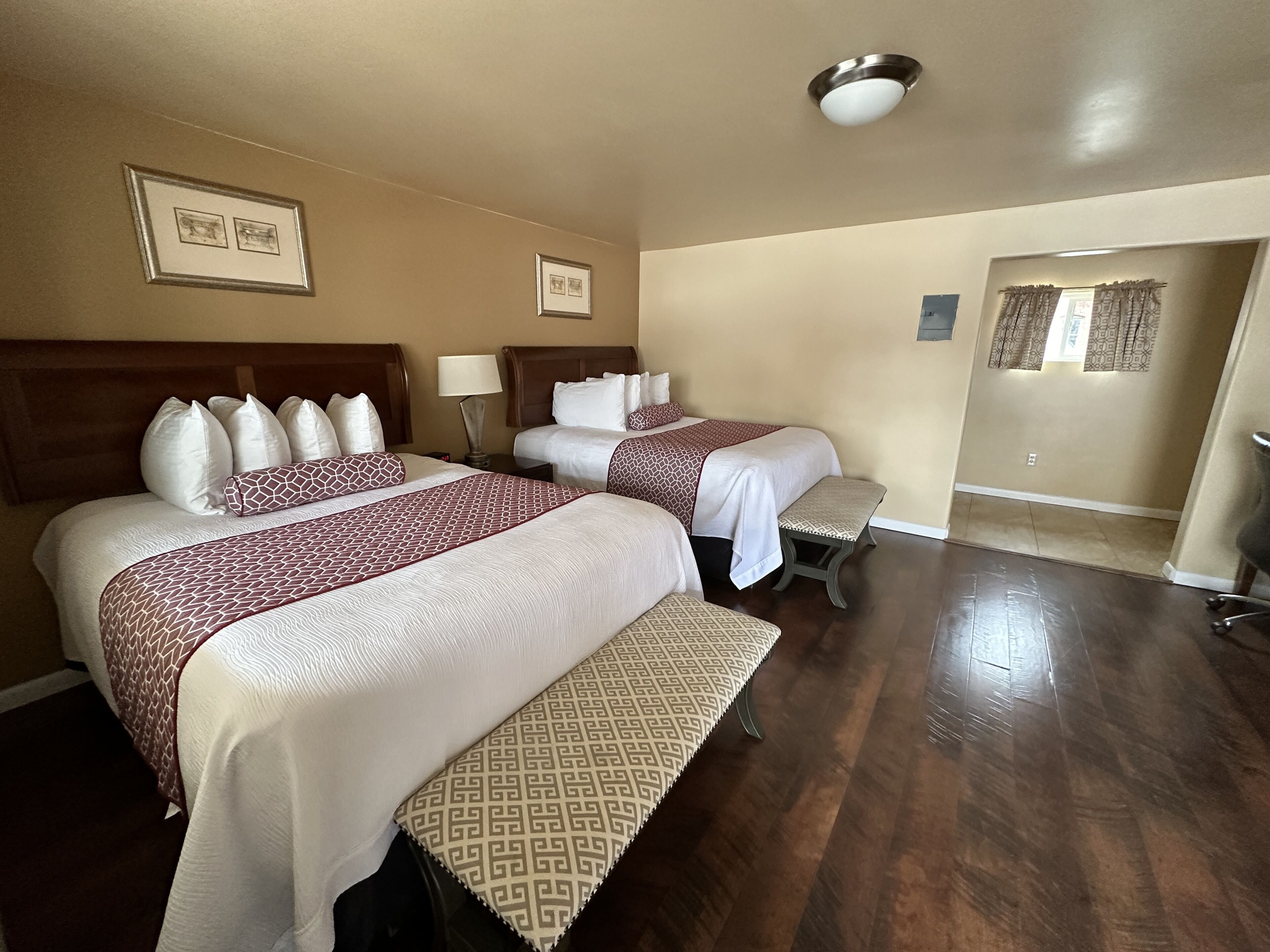 Habitación de hotel con dos camas, cabecera de madera, un banco y una puerta que da a otra habitación.