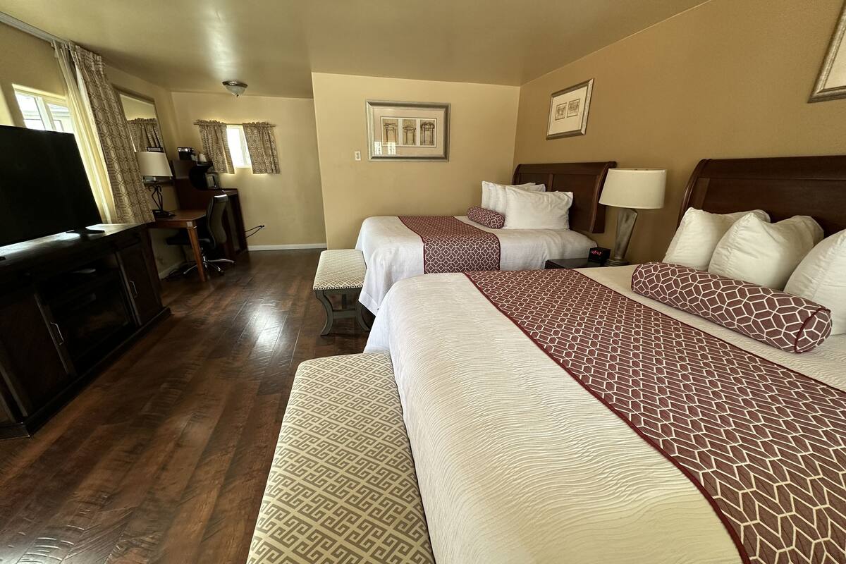 A hotel room with two beds, a desk, a television, and a window with curtains.