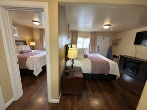 A hotel room with two beds, a TV, a fireplace, and a wooden floor.