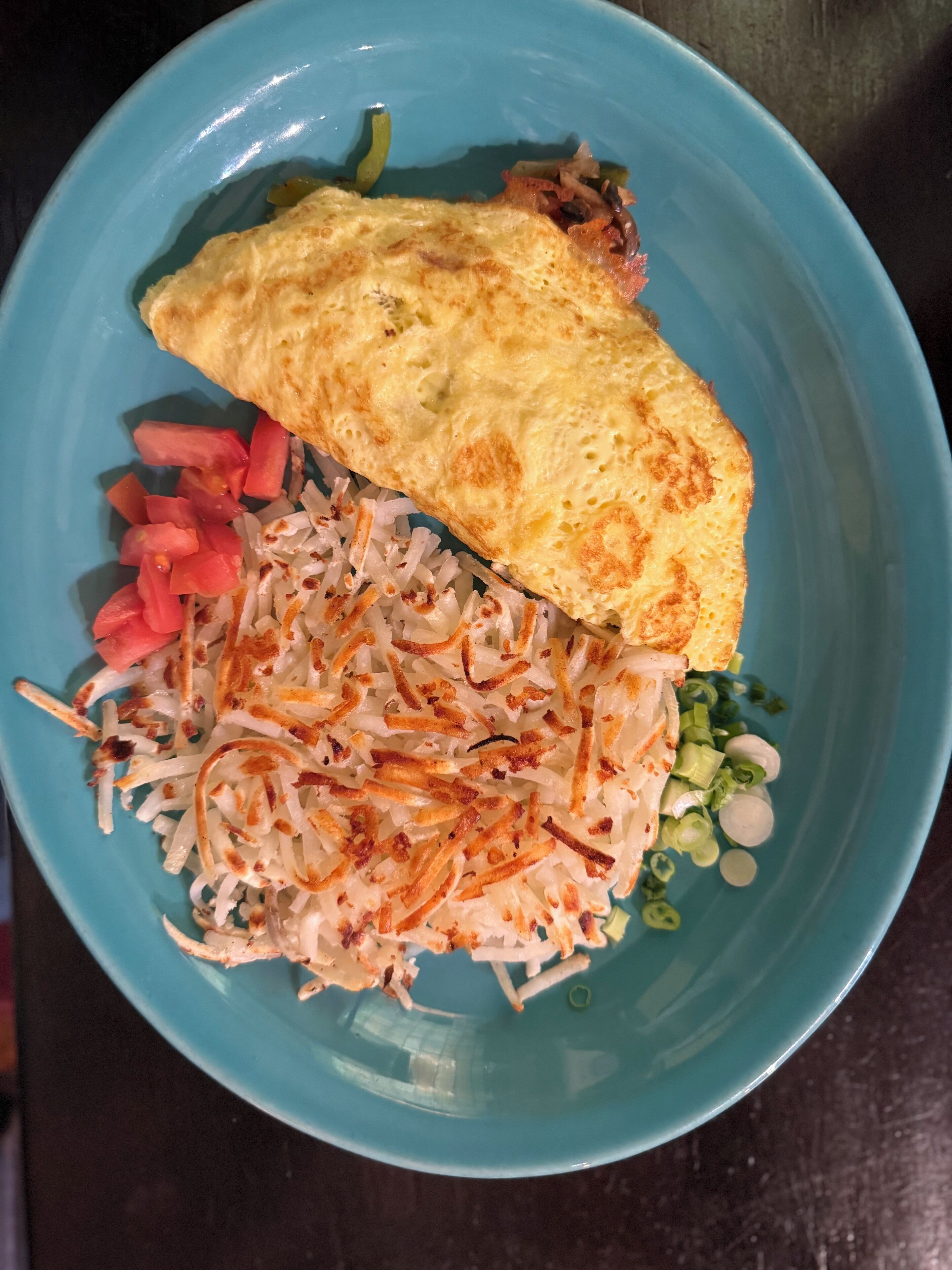 A blue plate with an omelette, sliced tomatoes, shredded cabbage, and green onions.