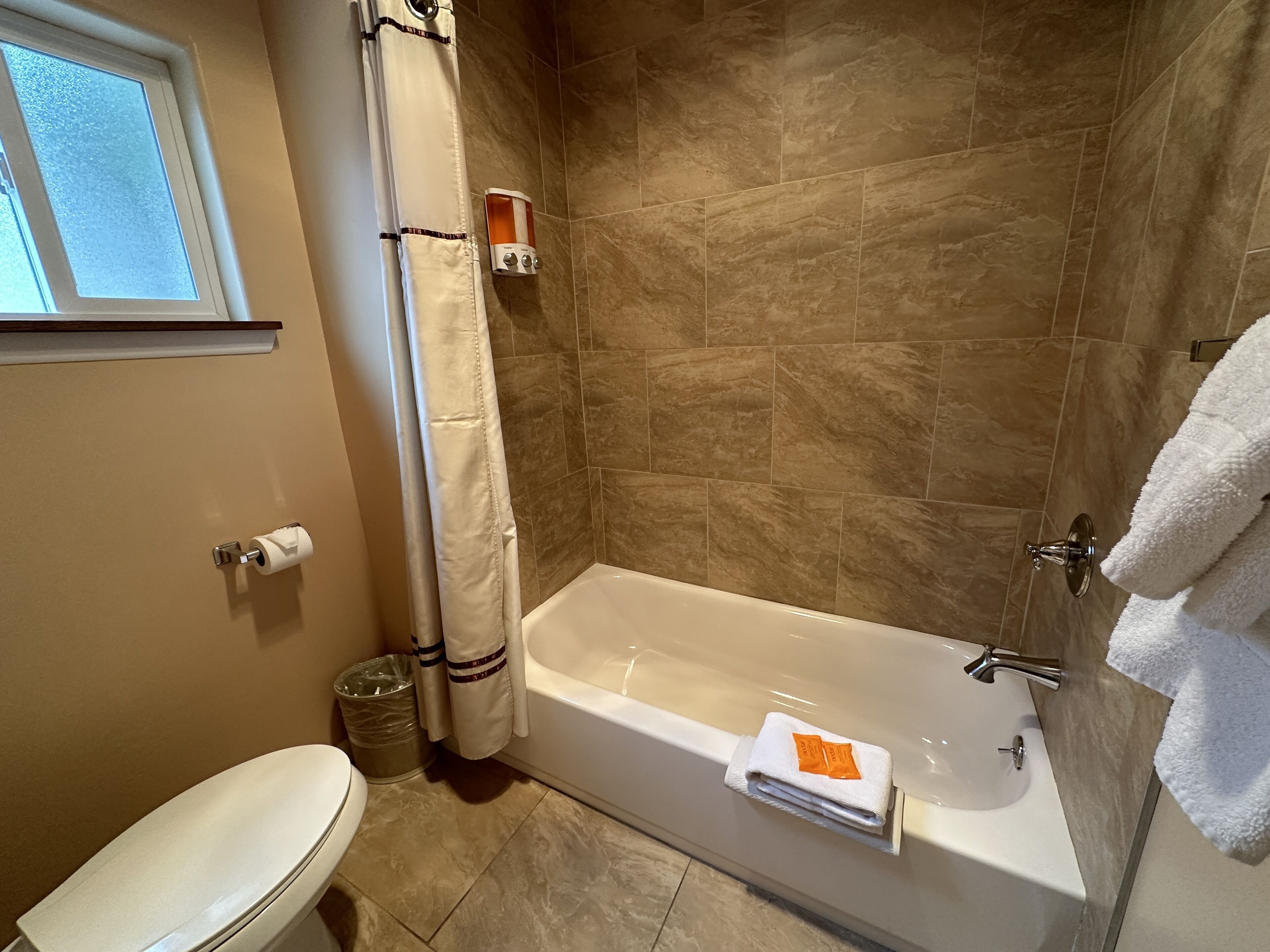 Une salle de bain avec une baignoire, des toilettes et une fenêtre.