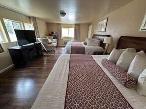 Habitación de hotel con una cama grande, un escritorio con televisor, una silla y una ventana con cortinas.