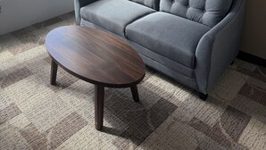 A modern office space with a grey sofa, a round wooden table, and a cityscape view through a large window. - Residence & Conference Centre - Calgary (Calgary)