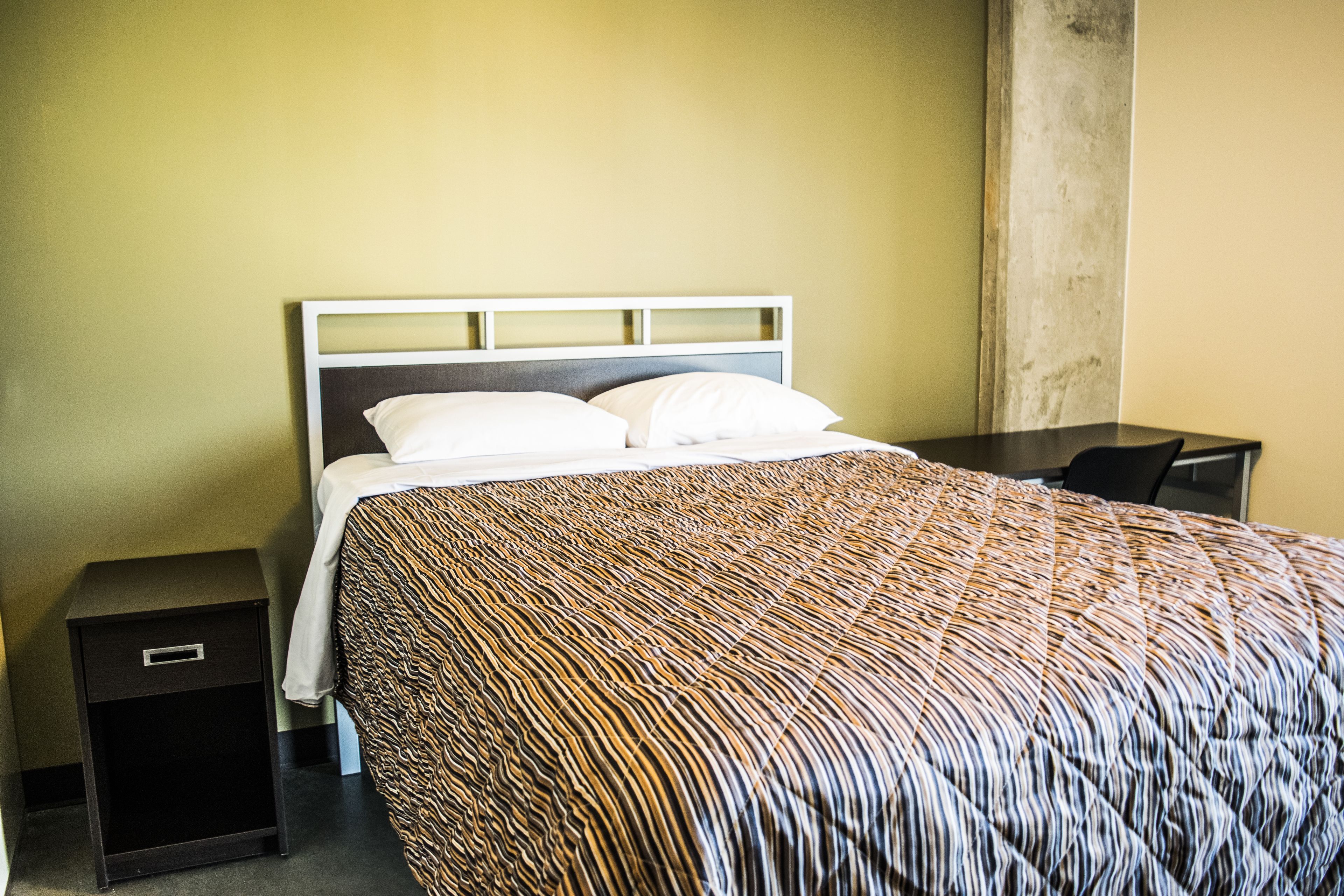 A hotel room with a bed, a nightstand, and a desk.