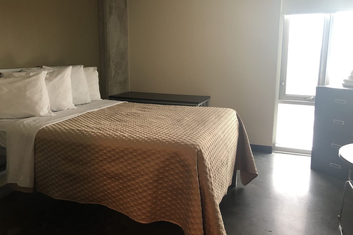 A hotel room with a bed, a bedside table, a dresser, and a window.
