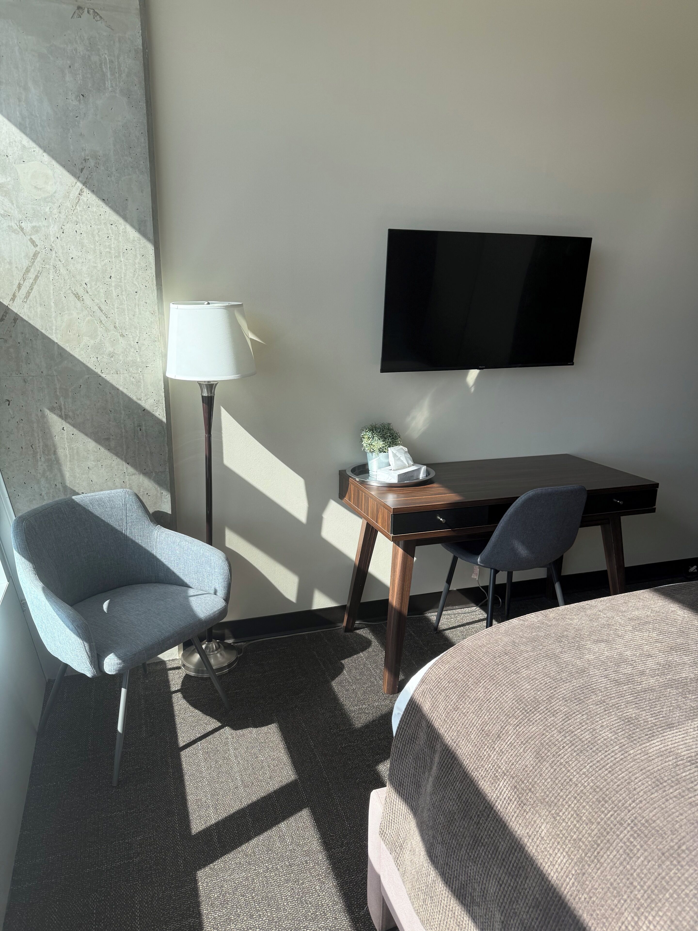 A hotel room with a bed, a desk, a chair, a TV, and a lamp.