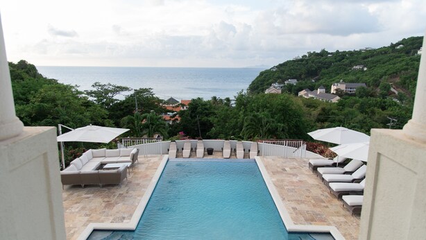 A swimming pool with lounge chairs and umbrellas, surrounded by greenery and overlooking a body of water. - Villa Hall (Gros Islet)