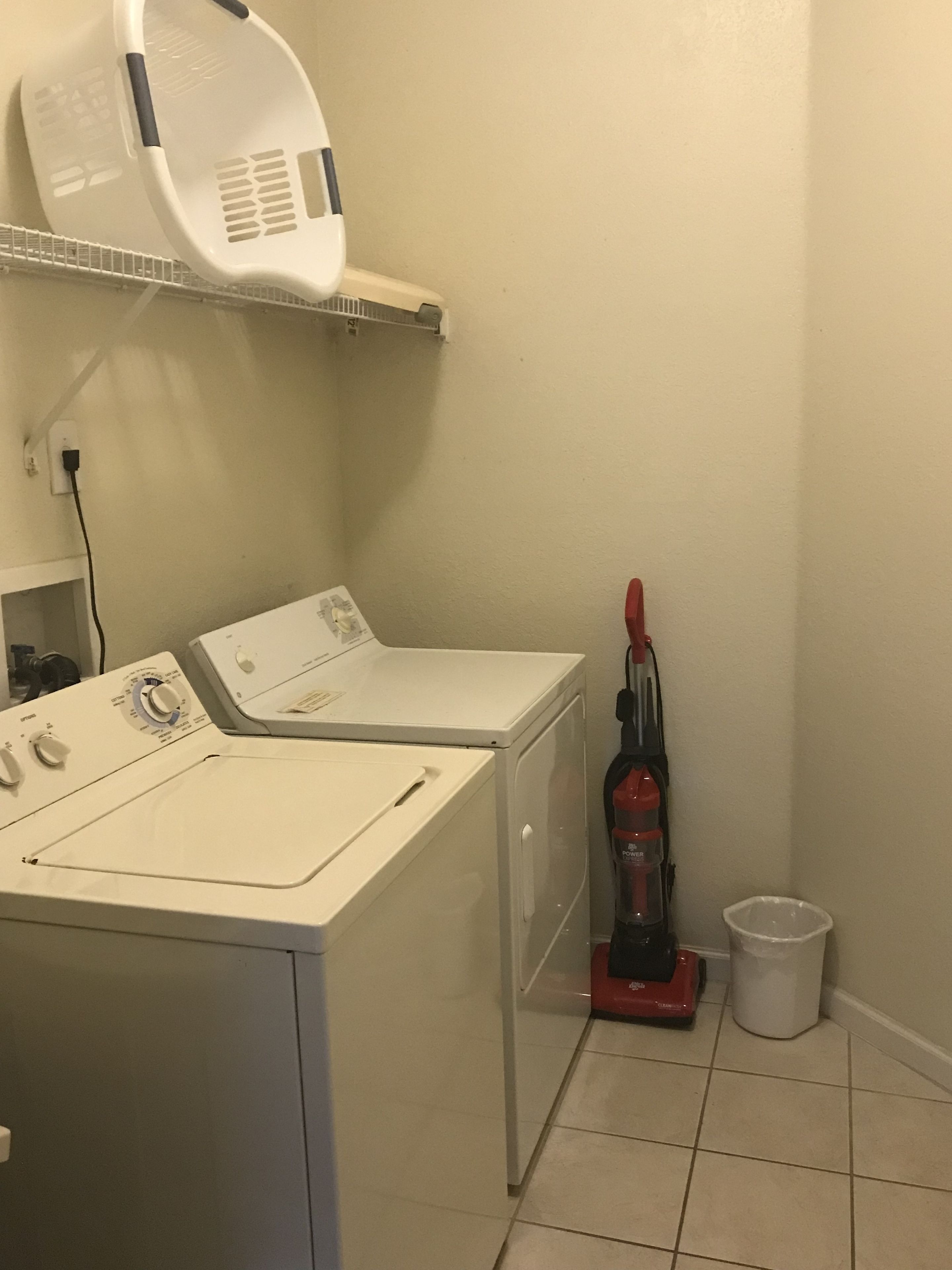 A laundry area with a washing machine, a dryer, a vacuum cleaner, and a trash bin.