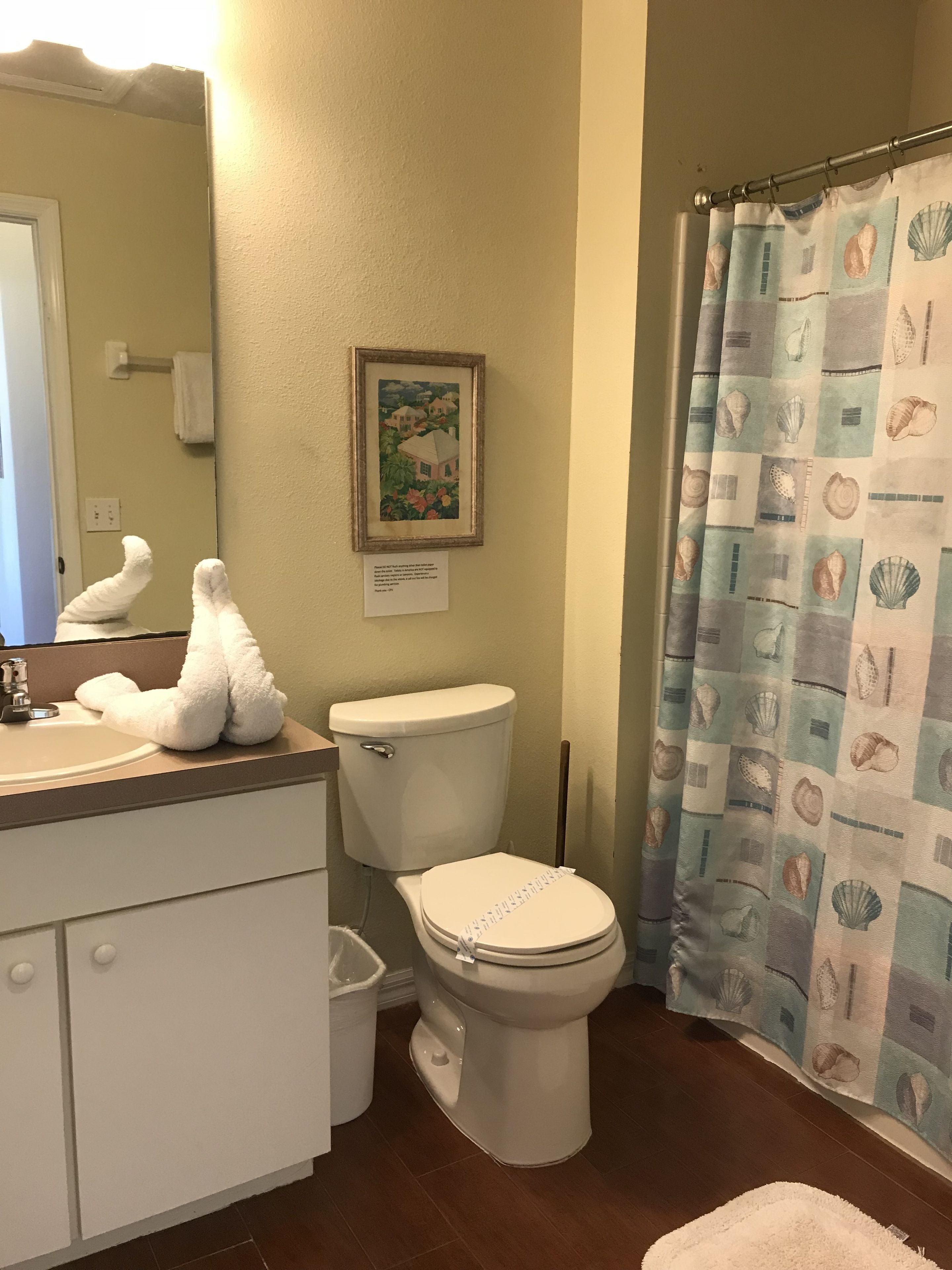 A bathroom with a toilet, sink, and a framed picture on the wall.