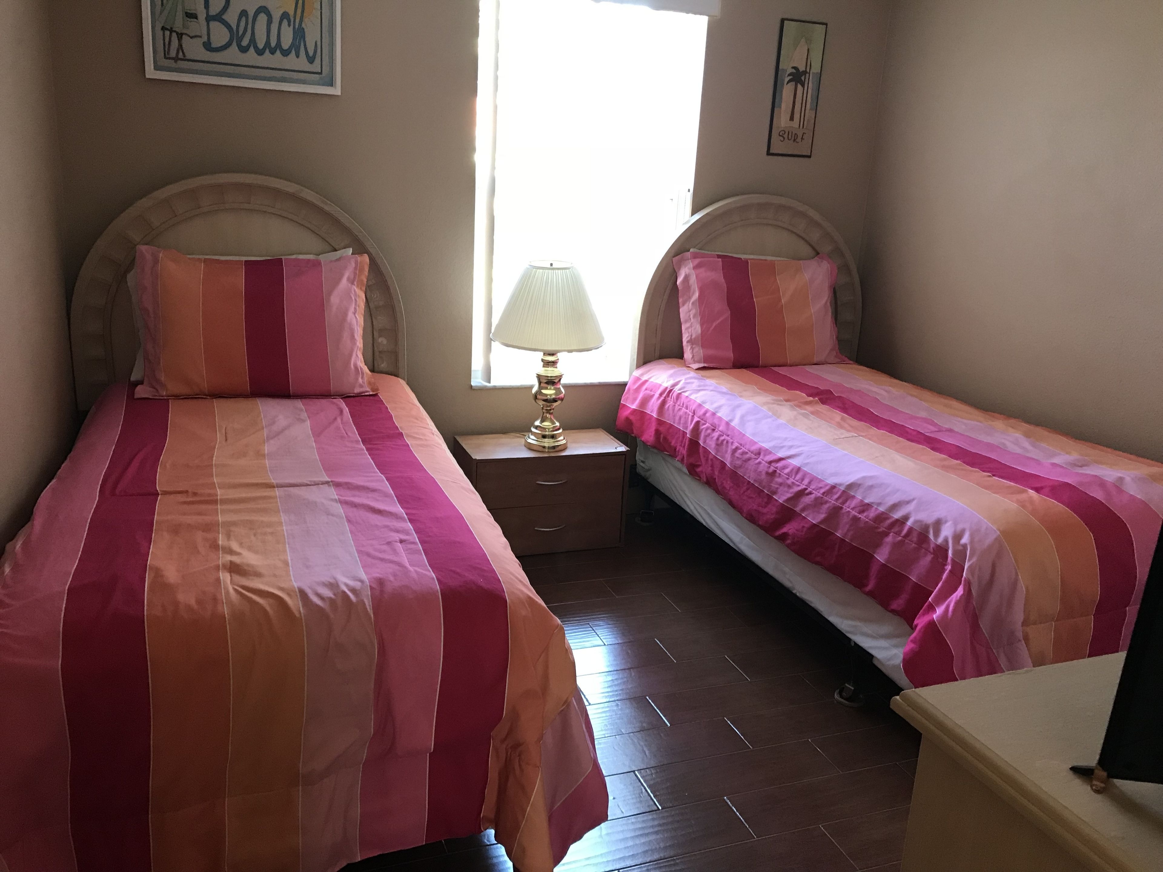 Une chambre à coucher avec deux lits, chacun doté de draps à rayures, une table de chevet avec une lampe et une fenêtre avec des rideaux.